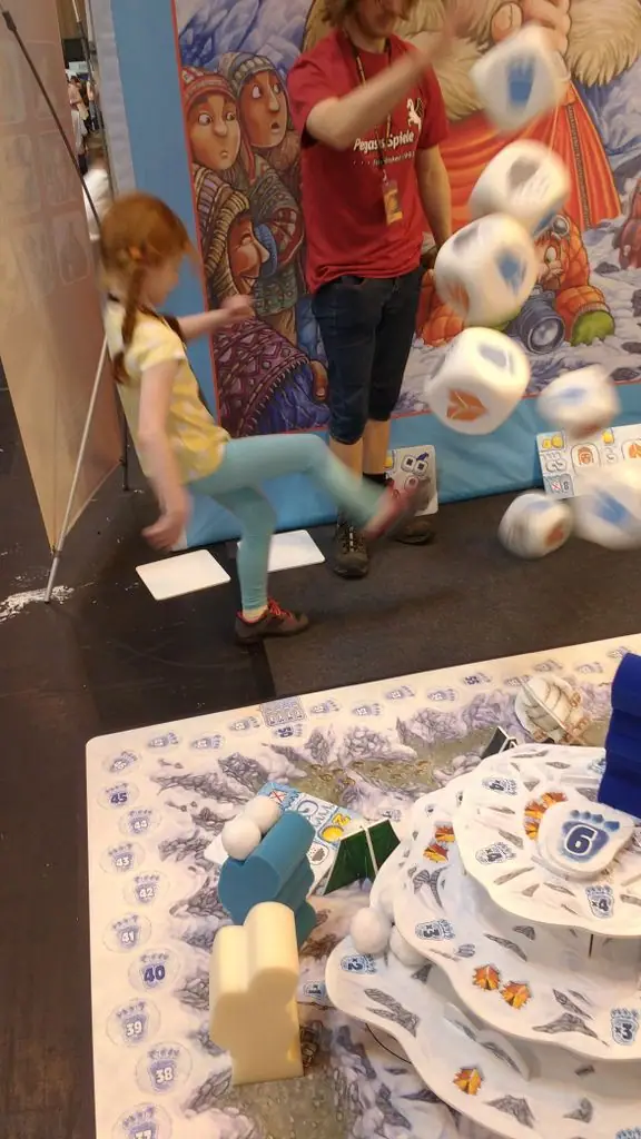 Action shot of my six year old daughter 'rolling' (kicking) the dice on Pegasus Spiele's giant demo set of Yeti at UK Games Expo 2016